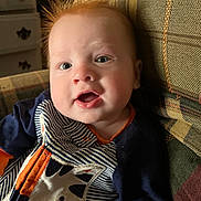 Simon is registered to the contest to win money with this photo: baby, child, face, red_hair, striped_clothing, animal_patch, couch, indoor, happy, smiling, portrait, closeup, furniture, pattern, young_child, infant, casual, seated, cute, cozy