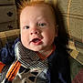 baby, child, face, red_hair, striped_clothing, animal_patch, couch, indoor, happy, smiling, portrait, closeup, furniture, pattern, young_child, infant, casual, seated, cute, cozy