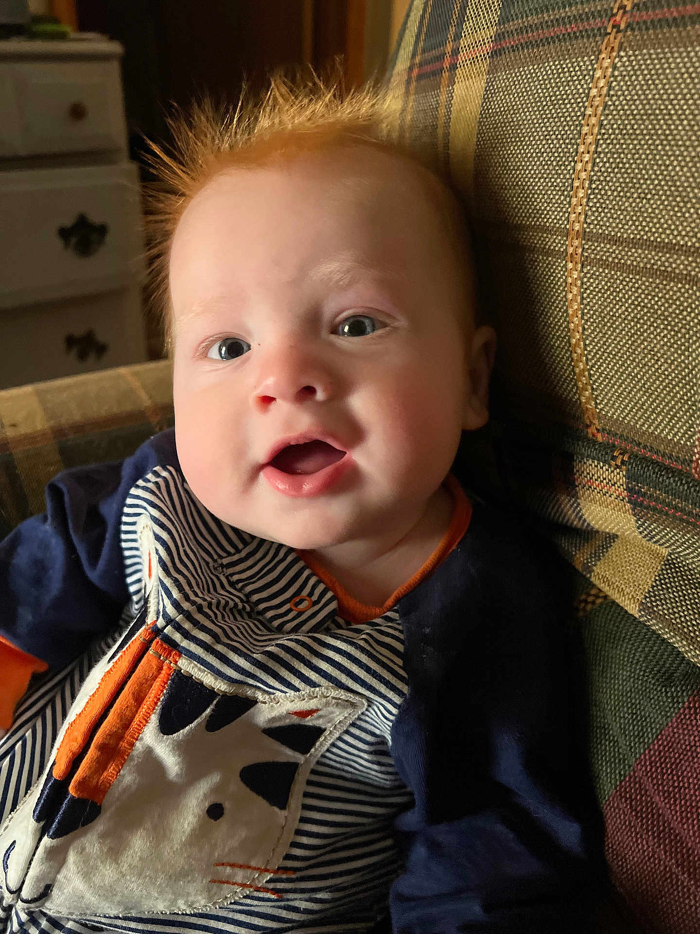 Simon is registered to the contest to win money with this photo: baby, child, face, red_hair, striped_clothing, animal_patch, couch, indoor, happy, smiling, portrait, closeup, furniture, pattern, young_child, infant, casual, seated, cute, cozy