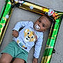 baby, barefoot, cartoon_animals, casual_clothing, child, concrete_floor, cute, expression, face, inflatable_frame, jungle_theme, lying_down, outdoor, pacifier, person, shorts, simba, sweatshirt, toddler, young_child