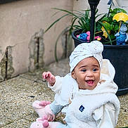 Chelsea participe au concours pour gagner de l'argent avec cette photo : baby, bunny_slippers, casual_clothing, child, cozy, cute, decorations, expression, green_mat, happy, hoodie, outdoor, plant_pot, plants, playful, sitting, slippers, smiling, stone_floor, turban