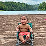 toddler, child, beach, sand, lake, water, trees, sky, clouds, greenery, swim_trunks, chair, outdoor, nature, summer, barefoot, portrait, sitting, curious, vacation