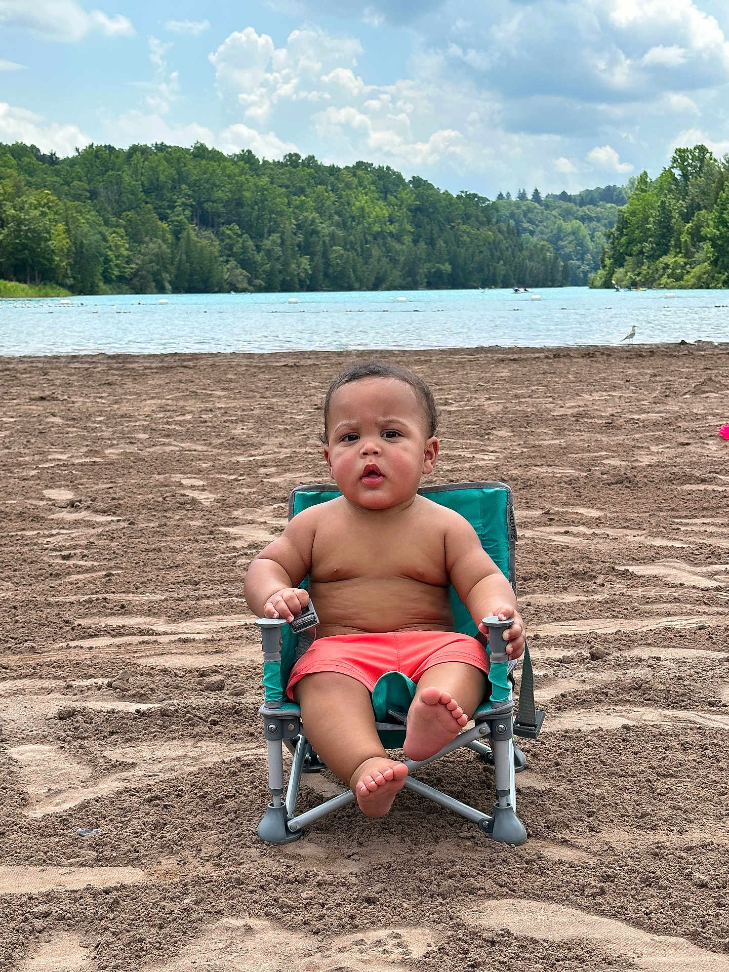 Ryker joined the competition — help win amazing prizes! toddler, child, beach, sand, lake, water, trees, sky, clouds, greenery, swim_trunks, chair, outdoor, nature, summer, barefoot, portrait, sitting, curious, vacation