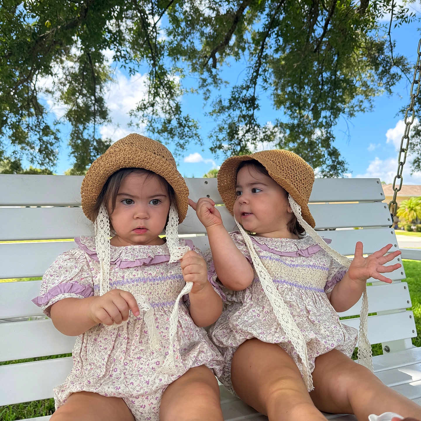 Gianna And Lianna is registered to the contest to win money with this photo: toddler, child, twins, matching_outfits, hat, straw_hat, sitting, swing_bench, outdoor, nature, tree, greenery, blue_sky, clouds, grass, summer, cute, expression, footwear, daytime