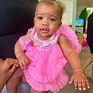 Makenzie is registered to the contest to win money with this photo: adult, baby, background, bracelet, child, clothing, curious, face, floor, hair_bow, hands, holding, indoor, other_children, people, person, pink_dress, play_area, smiling, tutu
