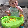 Preszley is registered to the contest to win money with this photo: baby, child, smiling, highchair, food, green_vegetables, yellow_vegetables, indoor, carpet, kitchen, sitting, safety_1st, clothing, short_sleeve, face, cute, happy, messy, meal, person