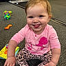 baby, carpet, child, colorful, cute, expression, floor, fun, happy, indoor, leopard_print, person, pink_clothing, playful, sitting, smiling, toddler, tongue_out, toys, young_child