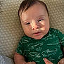 baby, infant, child, face, onesie, green_clothing, alligator_print, lying_down, blanket, textured_background, hand, finger, hair, skin, sunlight, portrait, closeup, expression, indoors, cozy