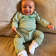 Kareem is registered to the contest to win money with this photo: baby, child, smiling, pajamas, striped_clothing, socks, couch, cushion, indoor, happy, person, infant, seated, cozy, home, portrait, cute, young_child, relaxed, comfortable
