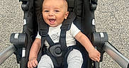 Kareem is registered to the contest to win money with this photo: baby, child, stroller, smile, happy, outdoor, pavement, clothing, infant, seatbelt, person, footwear, sock, cute, portrait, babywear, transport, wheel, hand, head