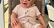 Kareem is registered to the contest to win money with this photo: baby, casual, chair, child, clothing, cute, drool, fashion, feet, happy, infant, outdoor, person, porch, relaxed, seat, smiling, sunglasses, sunlight, wicker