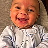 Kareem joined the competition — help win amazing prizes! baby, smiling, infant, onesie, indoor, happy, cute, child, face, skin, hand, lying_down, patterned_clothing, young_child, portrait, warm_lighting, soft_surface, closeup, joyful, expressive