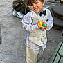 child, boy, smiling, vest, bow_tie, plaid_shirt, beige_pants, plastic_eggs, outdoor, concrete, bench, casual, portrait, happy, cute, young, fashion, playful, hands, standing