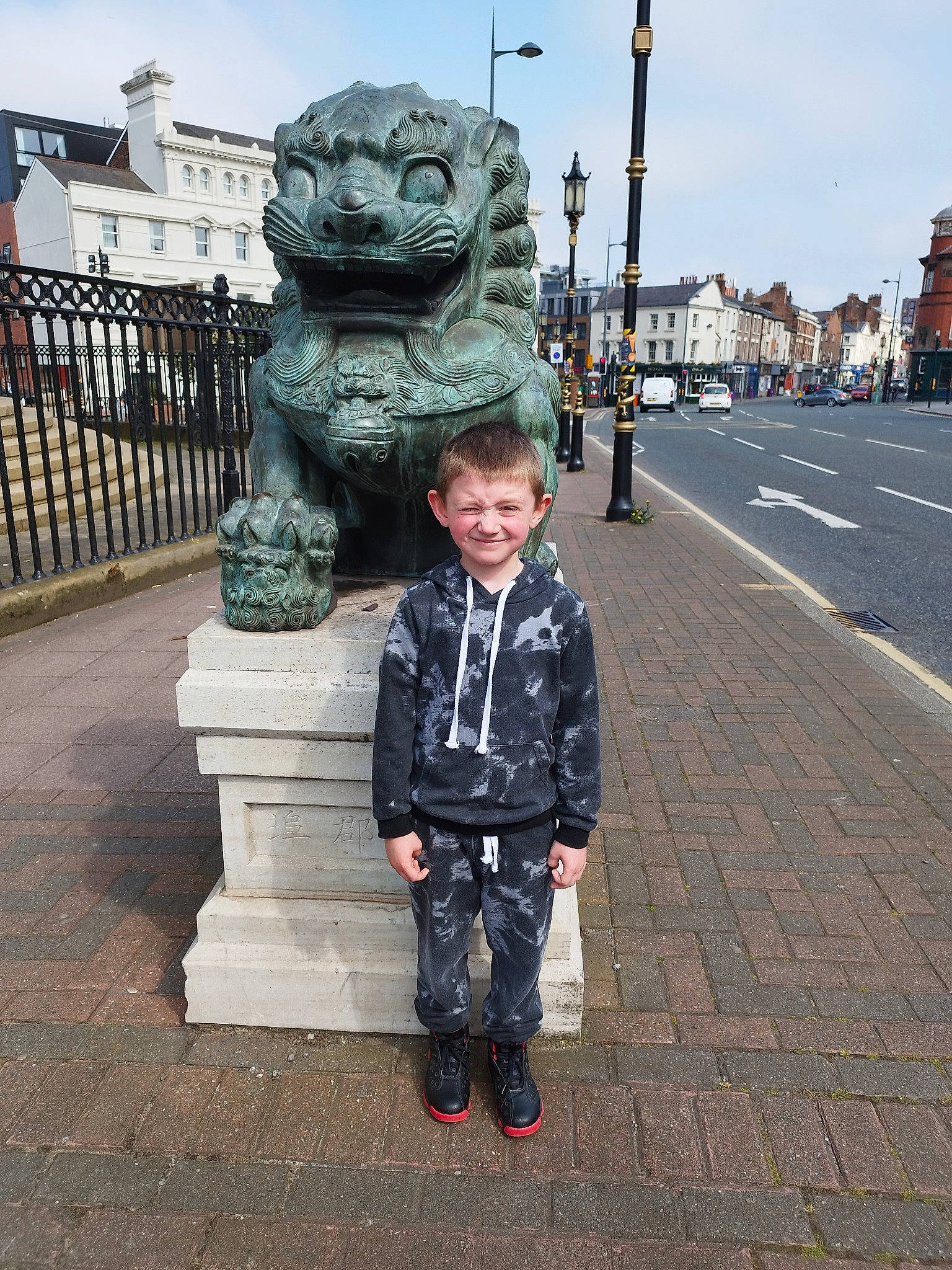 Benjamin is registered to the contest to win money with this photo: art, asphalt, building, car, city, fence, fun, joy, pedestrian, person, road, road_surface, sculpture, sidewalk, sky, smile, statue, street, toddler, tourism