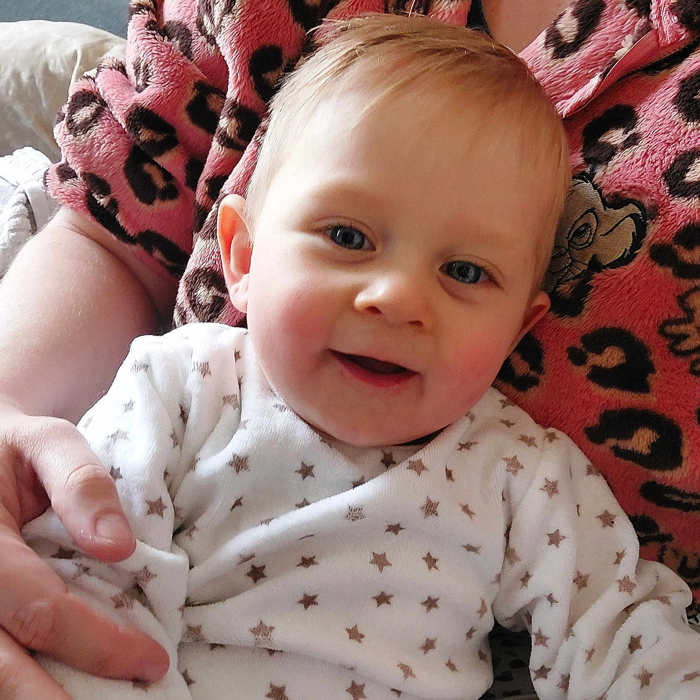 Timélio participe au concours pour gagner de l'argent avec cette photo : arm, baby, blue_eyes, caregiver, child, close_up, cuddly, face, hand, happy, indoor, infant, leopard_print, onesie, pink_robes, portrait, sitting, skin, smiling, star_pattern