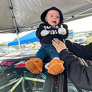 Weston joined the competition — help win amazing prizes! automobile, baby, bear_slippers, car, child, clothing, cute, daytime, expression, hands, hoodie, jeans, outdoor, parking_lot, person, racecar, smile, support, tent, vehicle