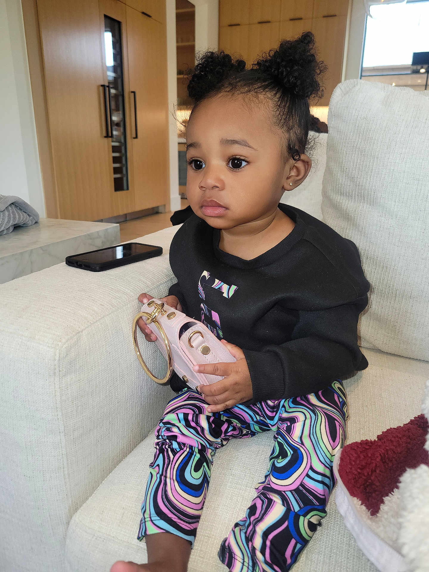 Airalynn is registered to the contest to win money with this photo: toddler, child, indoor, sitting, couch, purse, curly_hair, black_sweatshirt, colorful_pants, fashion, cute, portrait, home, furniture, person, young_child, expression, casual, relaxed, accessory