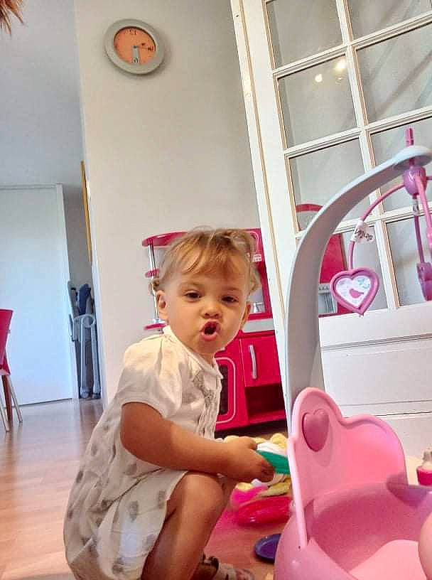 Ophélie a rejoint le concours — aidez-le/la à gagner de superbes lots ! baby, baby_toddler_clothing, child, clock, door, flooring, fun, hardwood, leisure, magenta, person, pink, riding_toy, room, sitting, skin, standing, t_shirt, toddler, toy