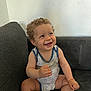 toddler, child, smile, curly_hair, onesie, sitting, couch, indoor, happy, face, skin, baby, furniture, arm, leg, wall, pattern, star, expression, person