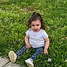 toddler, child, grass, outdoor, sitting, white_shirt, heart_pattern, leggings, shoes, concrete_path, greenery, cute, expression, young_child, nature, daylight, casual_clothing, playing, curly_hair, fun