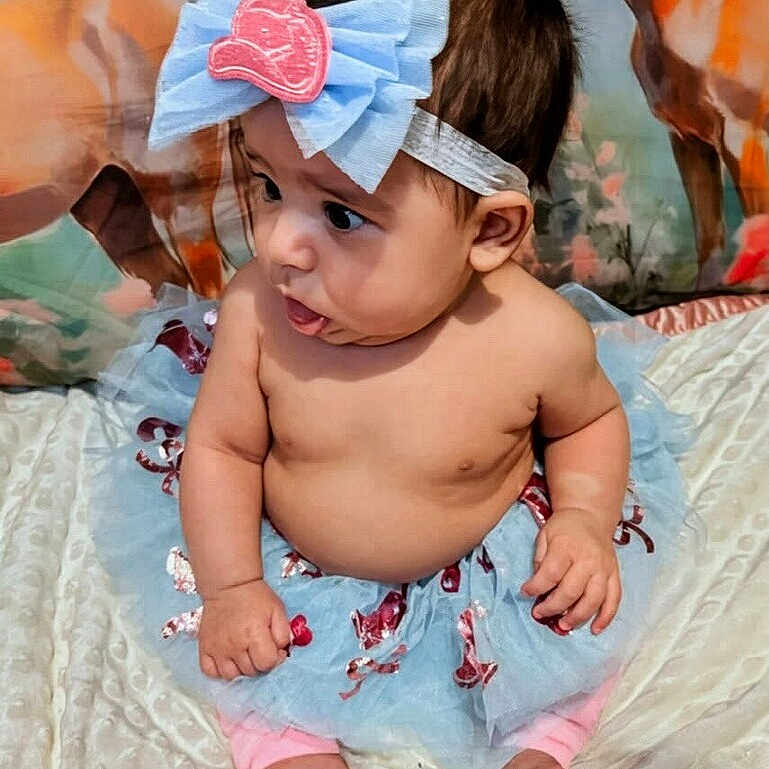 Gracie is registered to the contest to win money with this photo: baby, child, tutu, bow, headband, bare_chest, sitting, blanket, curious, indoors, footwear_none, pink_pants, cute, infant, portrait, decorative_background, animal_painting, soft_texture, skin, person