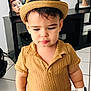 Aslan Castano joined the competition — help win amazing prizes! toddler, child, hat, yellow_shirt, blue_jeans, watch, indoor, floor_tiles, furniture, photo_frame, portrait, expression, standing, casual_clothing, young_child, home_interior, person, black_shelf, accessory, serious_face