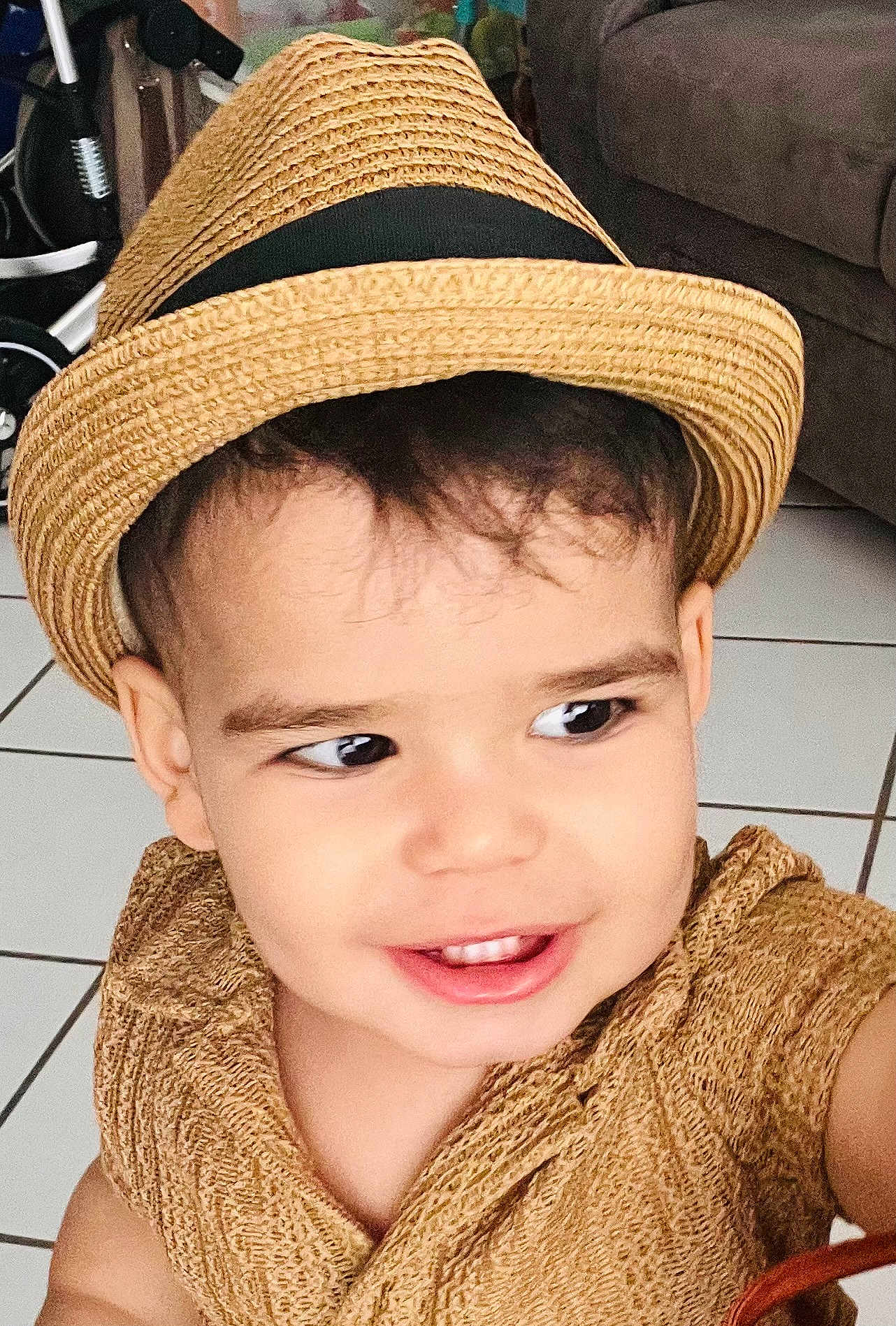 Aslan Castano joined the competition — help win amazing prizes! toddler, child, hat, straw_hat, smile, face, curly_hair, indoors, brown_clothing, textured_fabric, floor_tiles, living_room, couch, person, happy, cute, portrait, young_child, headwear, playful