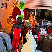 Molly joined the competition — help win amazing prizes! grinch_costume, child, dog, christmas_tree, holiday, living_room, window, blinds, couch, blanket, santa_hat, red_clothing, black_clothing, tile_floor, family, decorations, lights, indoor, celebration, people
