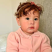 Andrea is registered to the contest to win money with this photo: toddler, child, curly_hair, pink_cardigan, headband, indoor, portrait, cute, young_child, face, sitting, expression, couch, soft_lighting, baby, person, clothing, earring, skin, hair_accessory