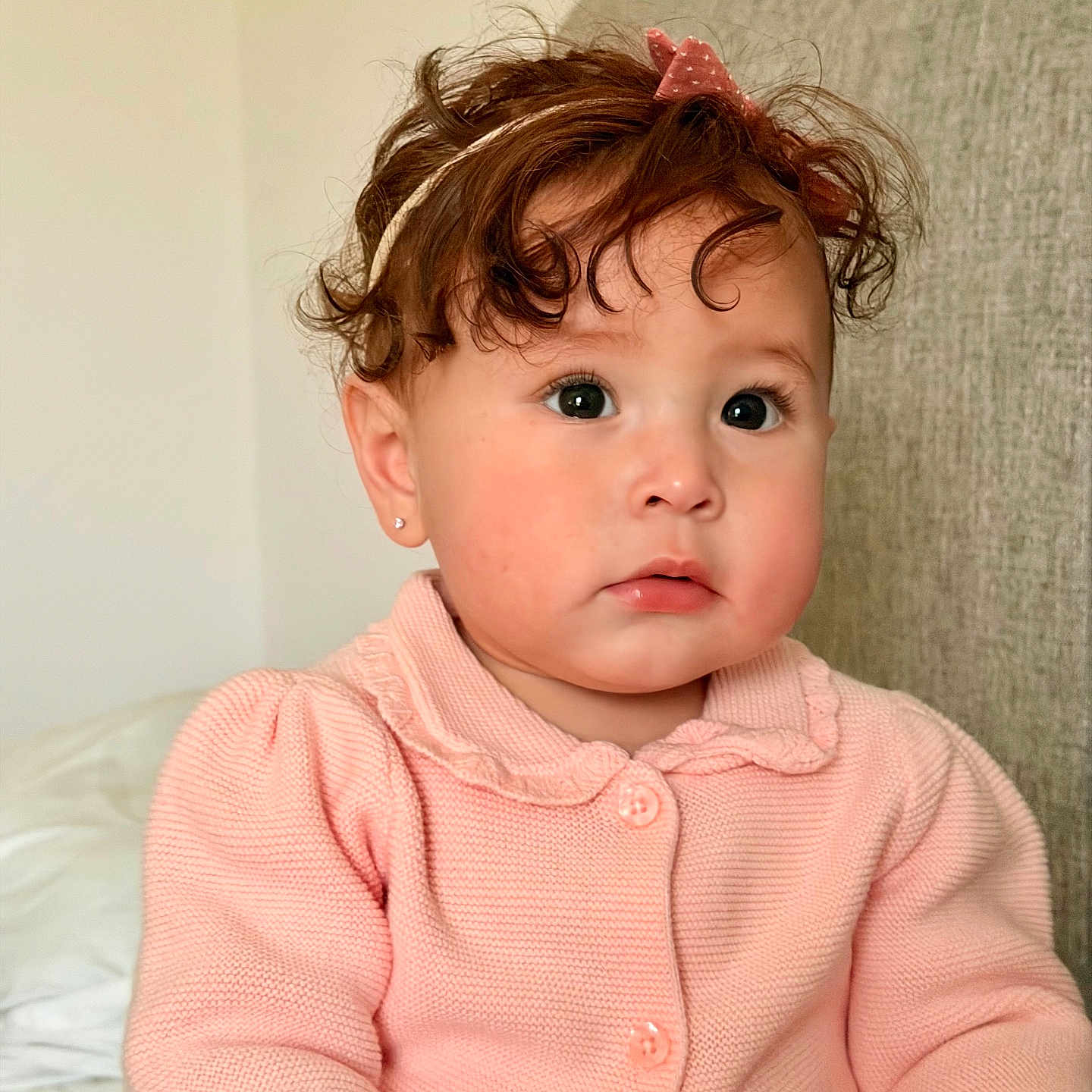 Andrea is registered to the contest to win money with this photo: toddler, child, curly_hair, pink_cardigan, headband, indoor, portrait, cute, young_child, face, sitting, expression, couch, soft_lighting, baby, person, clothing, earring, skin, hair_accessory