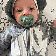 Yasser a rejoint le concours — aidez-le/la à gagner de superbes lots ! baby, infant, pacifier, hoodie, hat, face, eyes, nose, mouth, zipper, grey_clothing, white_print, patterned_background, close_up, portrait, newborn, small_hand, cute, laying_down, nursery