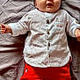 baby, infant, child, lying_down, white_shirt, red_shorts, smiling, face, hands, bed_sheet, clothing, cute, portrait, indoor, young_child, button_up, fabric, skin, relaxed, casual