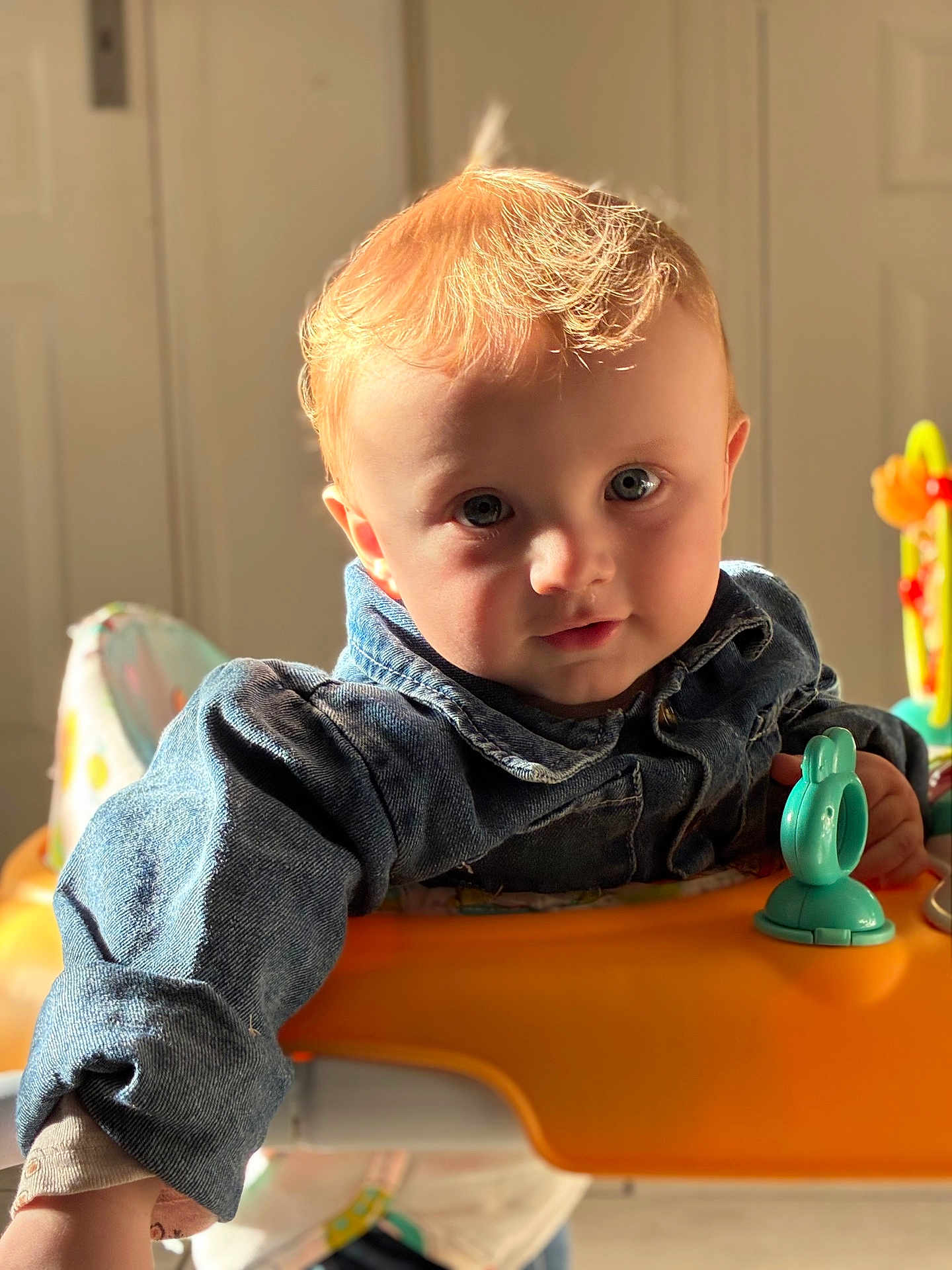 Edzio a rejoint le concours — aidez-le/la à gagner de superbes lots ! activity_center, baby, blue_eyes, child, close_up, curious_expression, cute, denim_jacket, face, indoor, natural_light, orange_tray, playtime, portrait, red_hair, seat, sunlight, teal_toy, toddler, toy