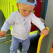 Jonas participe au concours pour gagner de l'argent avec cette photo : toddler, child, boy, cap, white_shirt, striped_pants, sneakers, playground, yellow_handle, outdoor, daylight, curious, exploring, colorful, plastic_structure, metal, greenery, shadow, casual_clothing, young_child