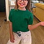 child, girl, smiling, green_sweater, white_pants, glasses, headband, indoor, living_room, wooden_floor, decor, furniture, posing, happy, portrait, casual_clothing, cheerful, fashion, young, person