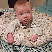 Aurelius is registered to the contest to win money with this photo: baby, infant, child, portrait, face, eyes, looking_at_camera, indoors, bedroom, bed, cushion, pillow, blanket, sweater, clothing, sitting, relaxed, floral_pattern, home, photography