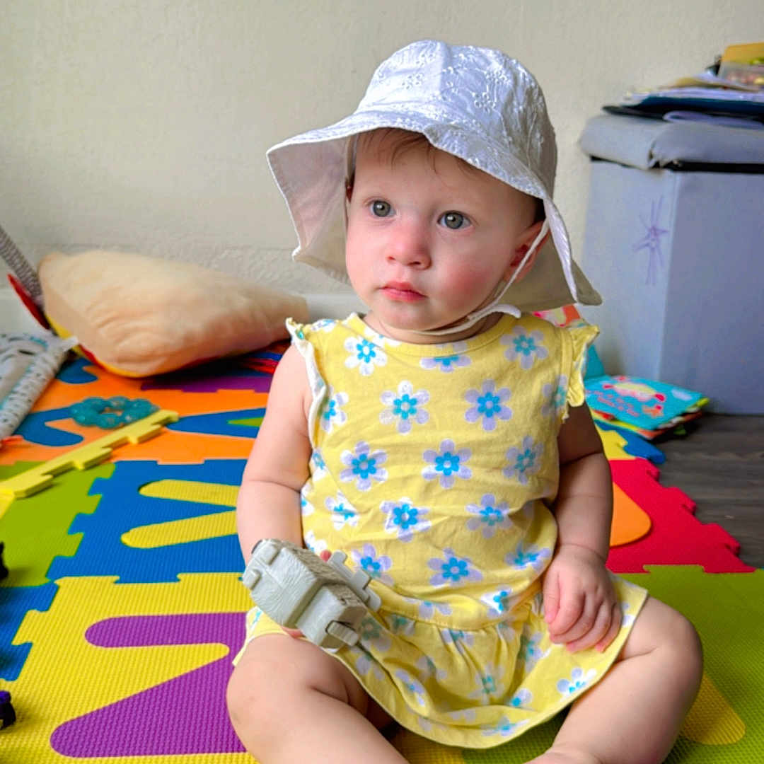 Hadaisha joined the competition — help win amazing prizes! baby, blue, child, colorful, dress, face, floor_mat, flower_pattern, foot, hand, hat, indoor, play_area, puzzle_mat, sitting, soft_light, toddler, toy, white, yellow