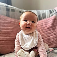 Mabel joined the competition — help win amazing prizes! baby, child, infant, crawling, pink_clothing, bib, socks, happy, smiling, face, hands, couch, pillows, blanket, indoor, cute, young_child, person, cozy, soft