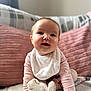 baby, child, infant, crawling, pink_clothing, bib, socks, happy, smiling, face, hands, couch, pillows, blanket, indoor, cute, young_child, person, cozy, soft