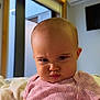 baby, infant, face, expression, serious, pink_clothing, blanket, bed, indoors, window, television, furniture, skin, head, earring, person, portrait, cute, child, room