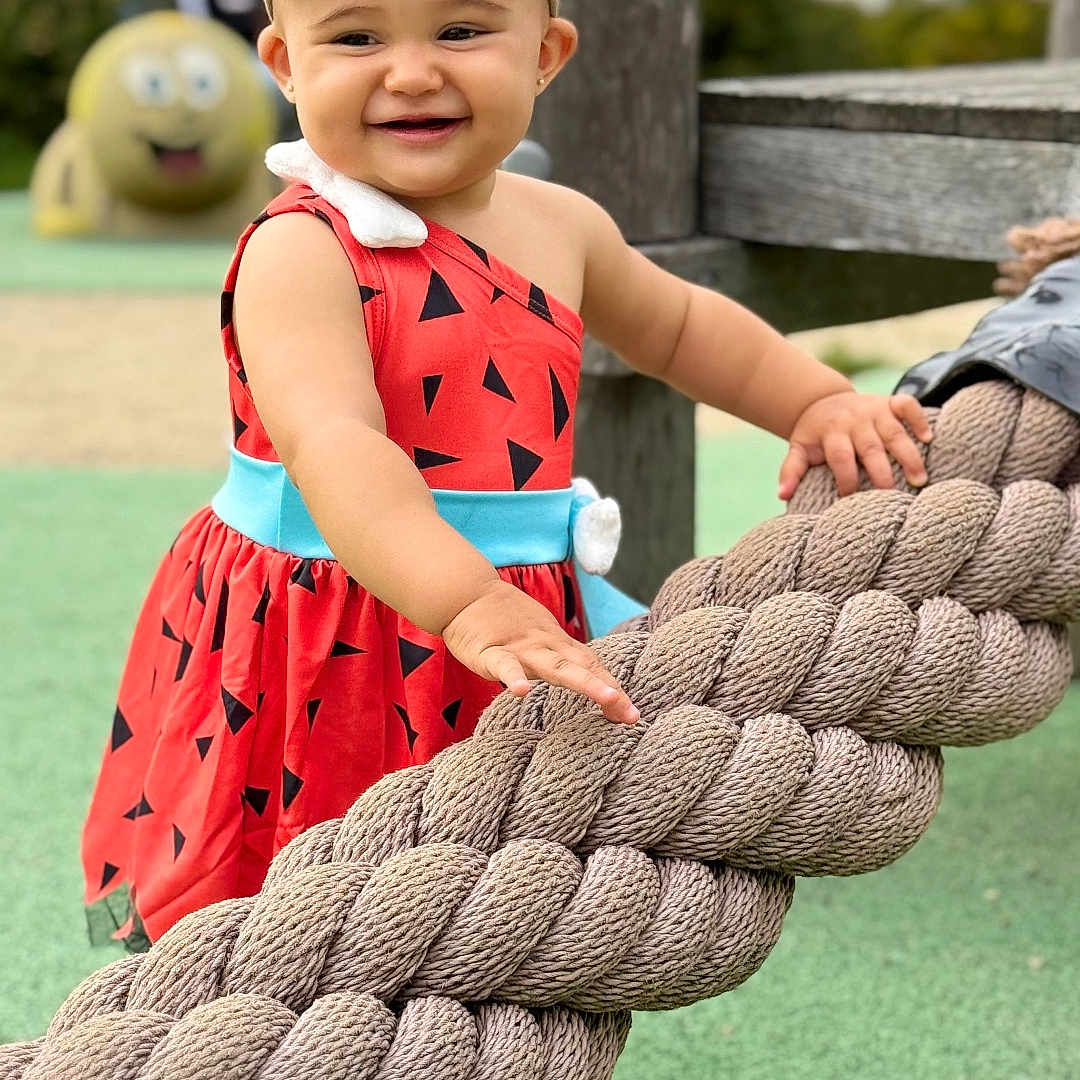 ísis a rejoint le concours — aidez-le/la à gagner de superbes lots ! background, barefoot, child, cute, daylight, dress, fun, green_ground, happy, headband, nature, outdoor, person, playground, recreation, rope, smiling, toddler, toy, wood