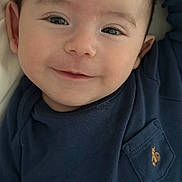 James is registered to the contest to win money with this photo: baby, smile, face, close_up, child, infant, blue_shirt, pocket, embroidery, skin, eyes, head, person, portrait, cute, young, happy, indoors, clothing, baby_face