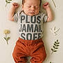 baby, sleeping, infant, clothing, pants, shirt, text_on_shirt, leaves, flowers, flat_lay, soft_texture, cute, peaceful, hands_up, socks, portrait, newborn, decorative, natural_elements, resting