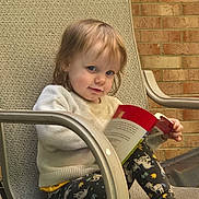Abigail joined the competition — help win amazing prizes! toddler, child, reading, book, chair, sweater, leggings, unicorn_pattern, barefoot, outdoor, brick_wall, texture, person, cute, portrait, relaxed, daylight, happy, seated, casual