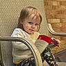 toddler, child, reading, book, chair, sweater, leggings, unicorn_pattern, barefoot, outdoor, brick_wall, texture, person, cute, portrait, relaxed, daylight, happy, seated, casual