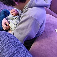 Tobias is registered to the contest to win money with this photo: baby, child, person, hoodie, couch, blanket, indoor, carpet, purple, seated, holding, young_person, casual_clothing, curly_hair, comfort, relaxed, home, infant, light, portrait