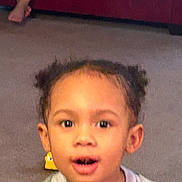 Ivanni joined the competition — help win amazing prizes! child, toddler, face, surprised, open_mouth, eyes, hair_puffs, ears, toy, carpet, living_room, couch, bare_foot, portrait, indoor, expression, clothing, person, young_child, smiling_ish