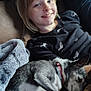 child, dog, couch, blanket, smile, resting, indoor, cozy, pet, fur, collar, relaxation, happy, comfort, leisure, person, portrait, casual, home, snuggle