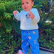 Alaia is registered to the contest to win money with this photo: blue_pants, casual_clothing, child, cute, flowers, garden, greenery, minnie_mouse, nature, outdoor, person, pink_sandals, plants, portrait, sidewalk, small_object, standing, sunlight, toddler, white_sweater