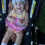 Sophia is registered to the contest to win money with this photo: baby, child, stroller, smile, bow, dress, socks, feet, legs, blanket, outdoor, happy, person, infant, cute, clothing, seat, baby_carrier, headwear, portrait